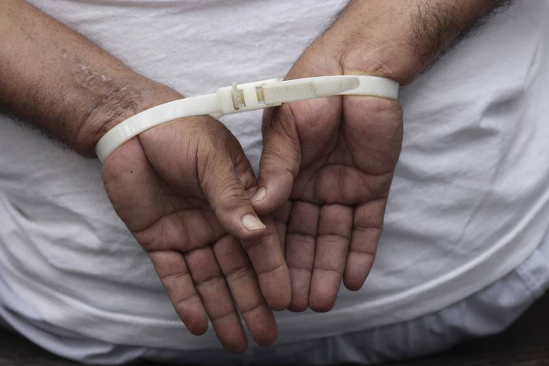 FILE - A handcuffed man, arrested for alleged gang connections, waits to be transferred to a prison at the police delegation of San Bartolo in Soyapango, El Salvador, Aug. 16, 2022. Congress voted on Dec. 14 to extend President Nayib Bukele’s emergency powers to crack down on gangs for the ninth time. (AP Photo/Salvador Melendez, File)